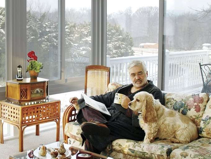 A man sits on a couch with a dog and reads a book