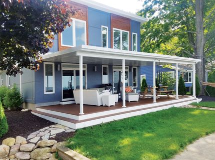 Blue and brown modern house with covered porch and deck overlooking green lawn.