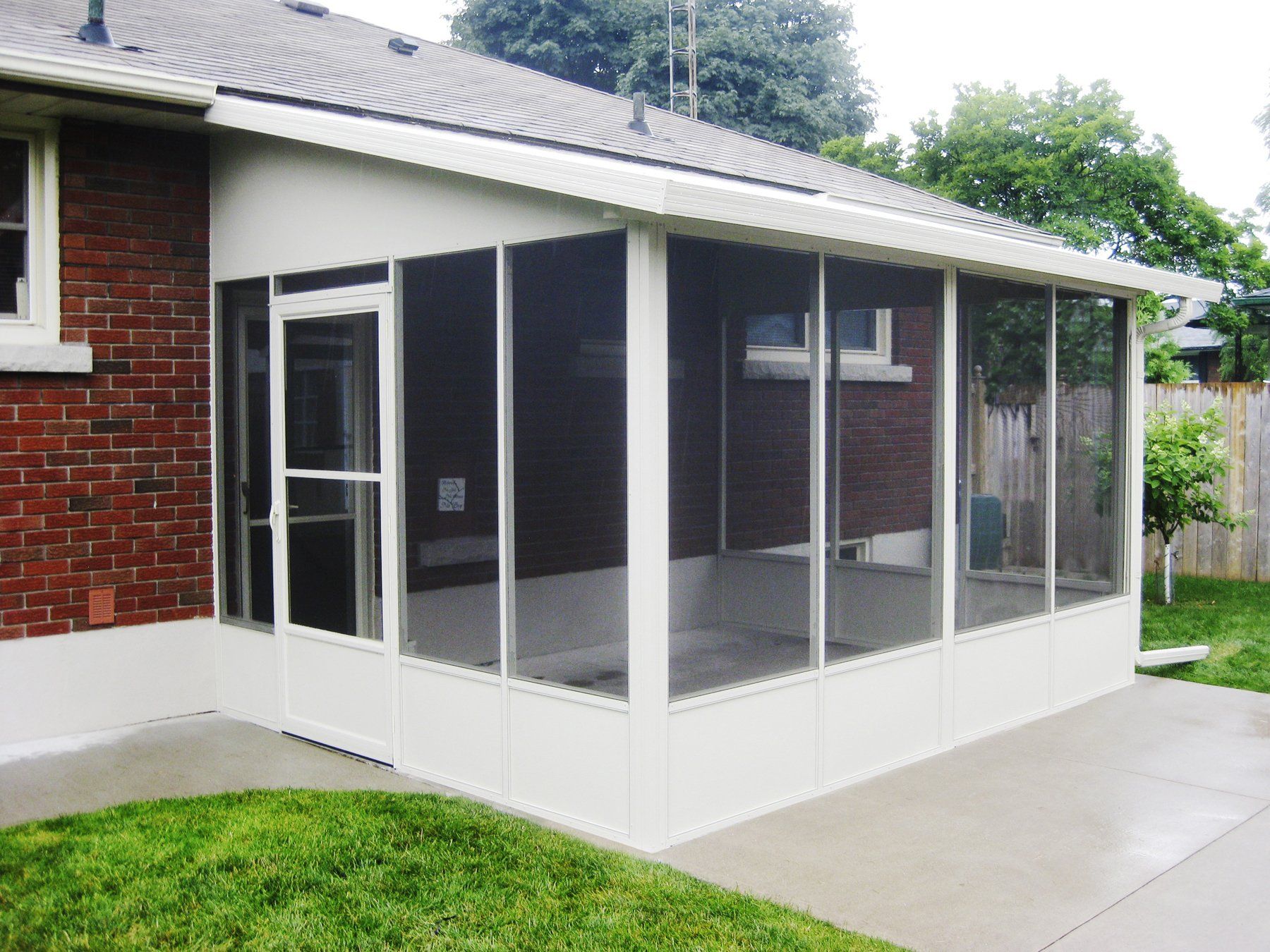 A screened in porch with a brick house in the background
