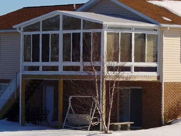 A house with a sunroom and a swing in the snow