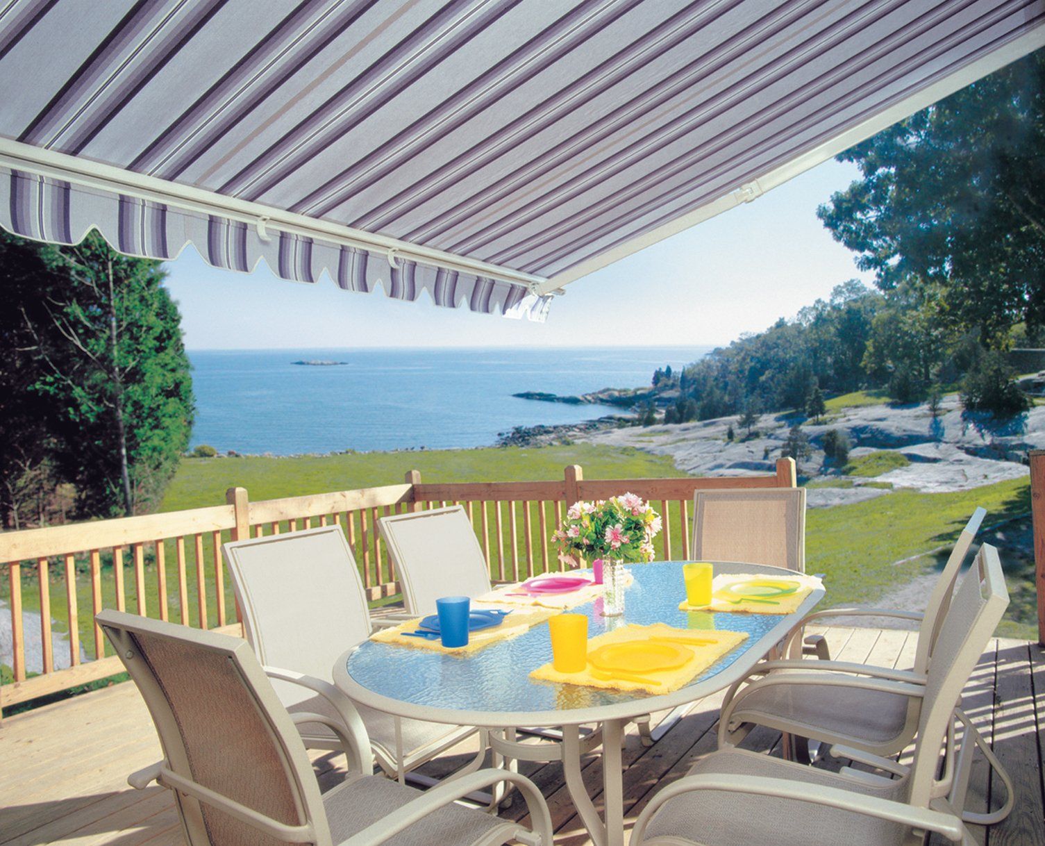 A patio with a table and chairs under an awning overlooking the ocean