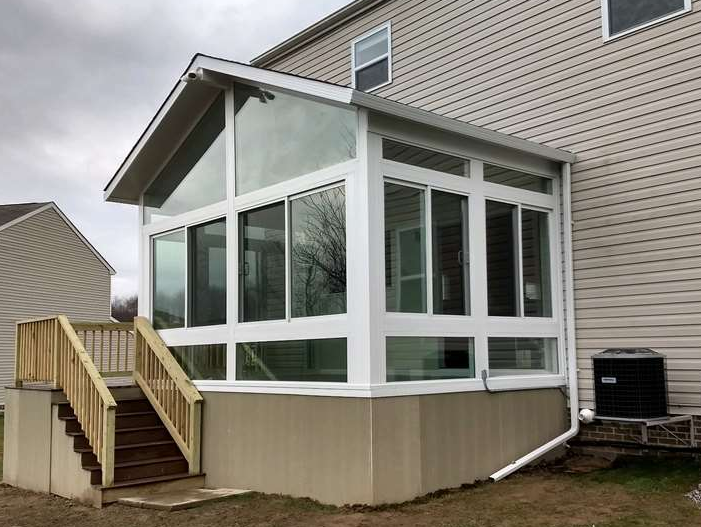 A sunroom with stairs leading up to it is attached to the side of a house.