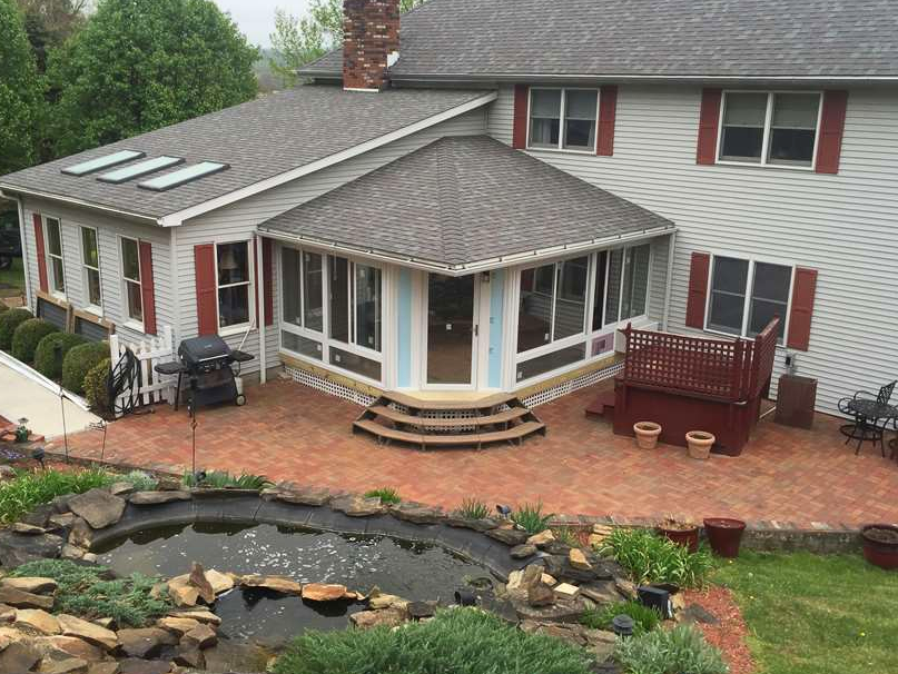 A house with a screened in porch and a pond in front of it.