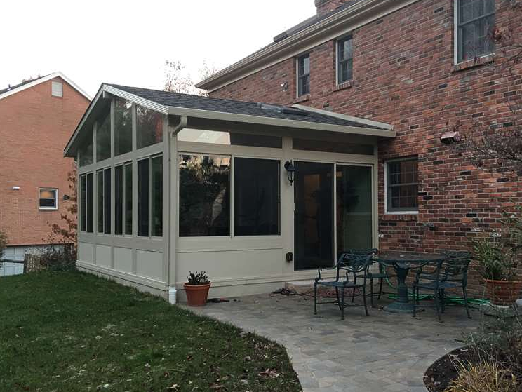 A screened in porch with a table and chairs in front of a brick house.