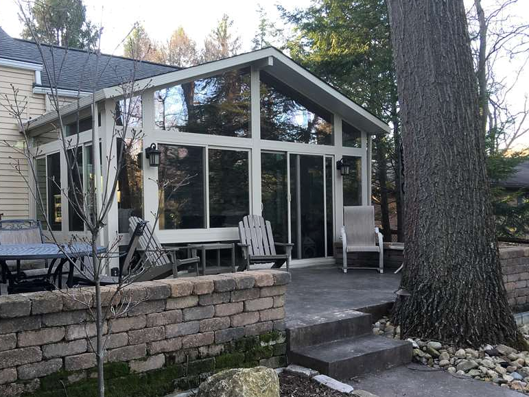 A house with a large sunroom and a tree in front of it.