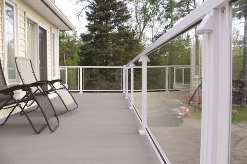 A deck with a glass railing and chairs on it.