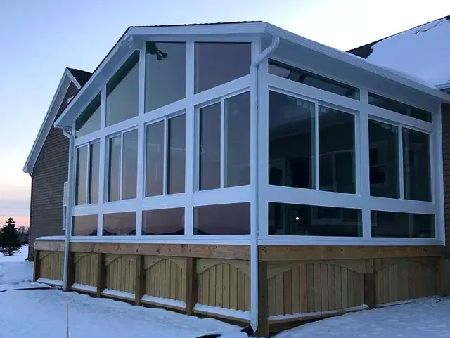 A sunroom with a lot of windows and a wooden deck in the snow.