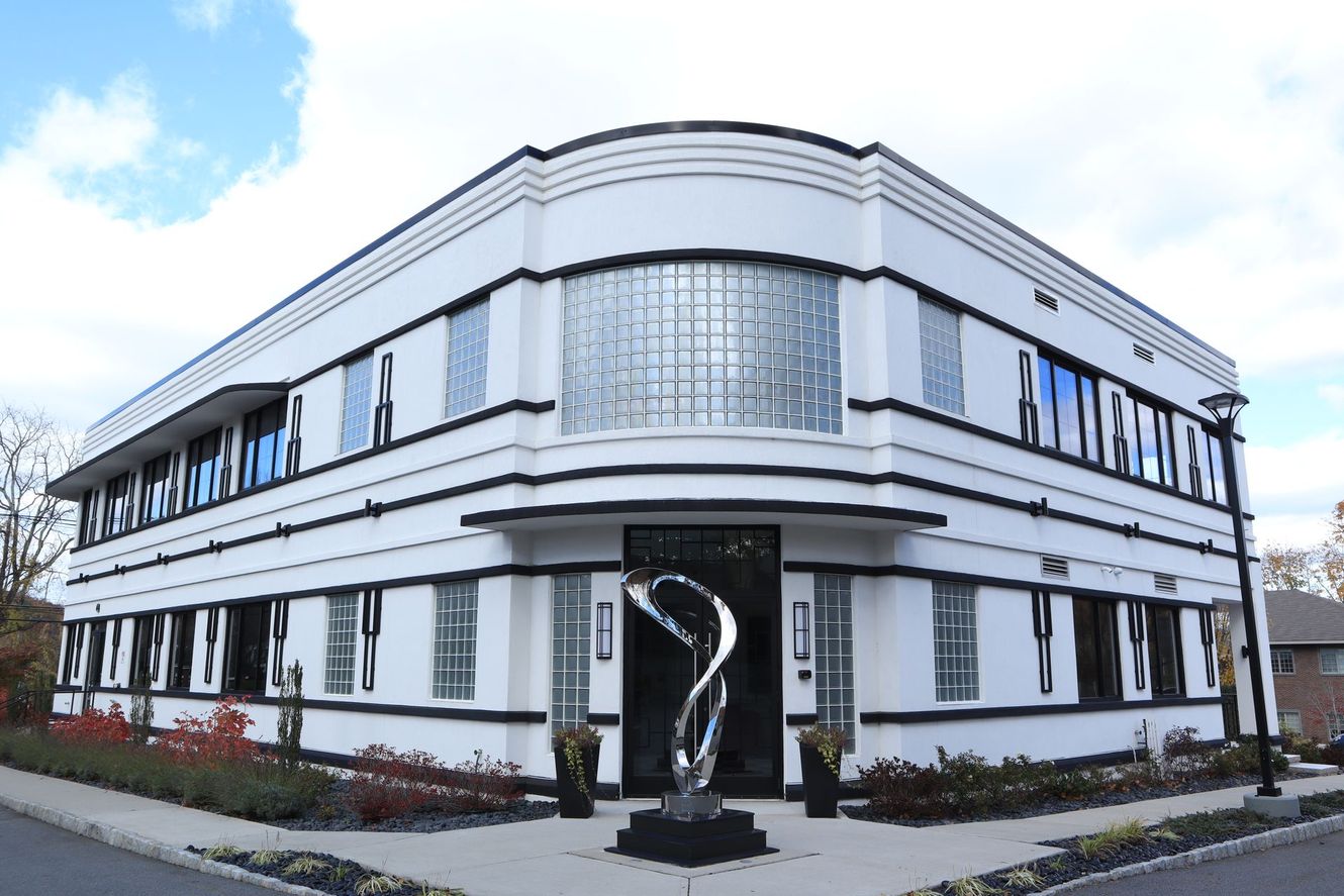 White and black Art Deco style building with glass sculpture at the entrance under a blue sky.