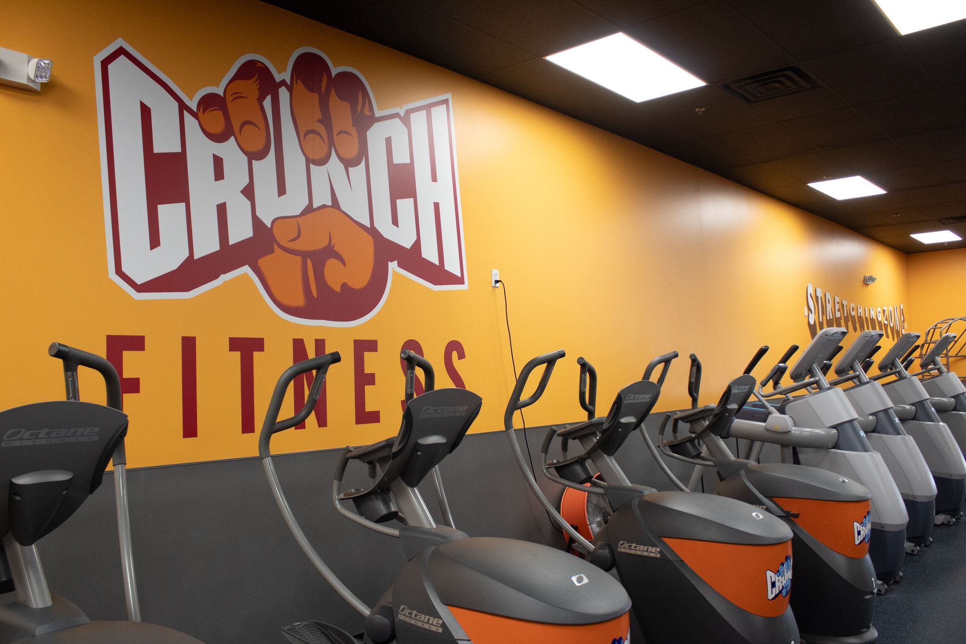 Crunch Fitness gym interior with rows of exercise machines and logo on the wall.