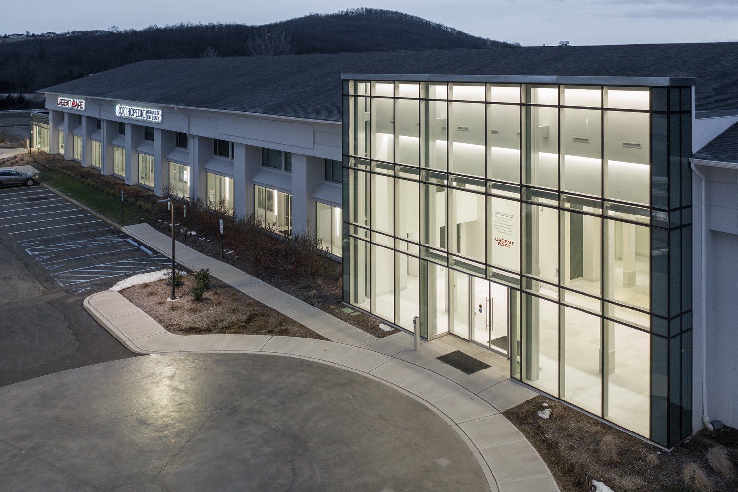 Modern building with glass entrance, dark roof, and landscaping at dusk.
