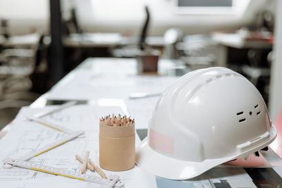 White hard hat, pencils, and blueprints on a desk in an office.