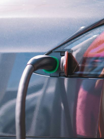 Electric vehicle charging, a dark car with a charging cable connected to its port, illuminated with green light.