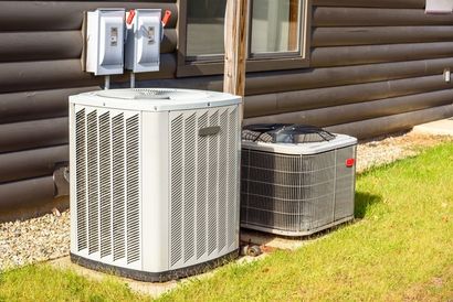 Two air conditioning units next to a building with electrical boxes above them, set on grass.