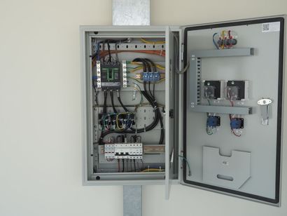 Open electrical panel with wires, circuits, and components mounted on a wall.