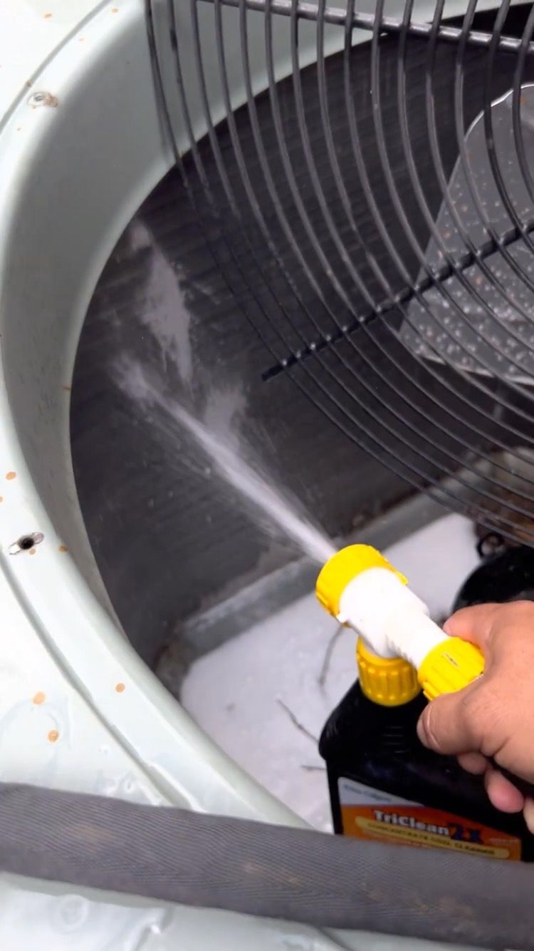 A person is cleaning an air conditioner with a spray bottle.