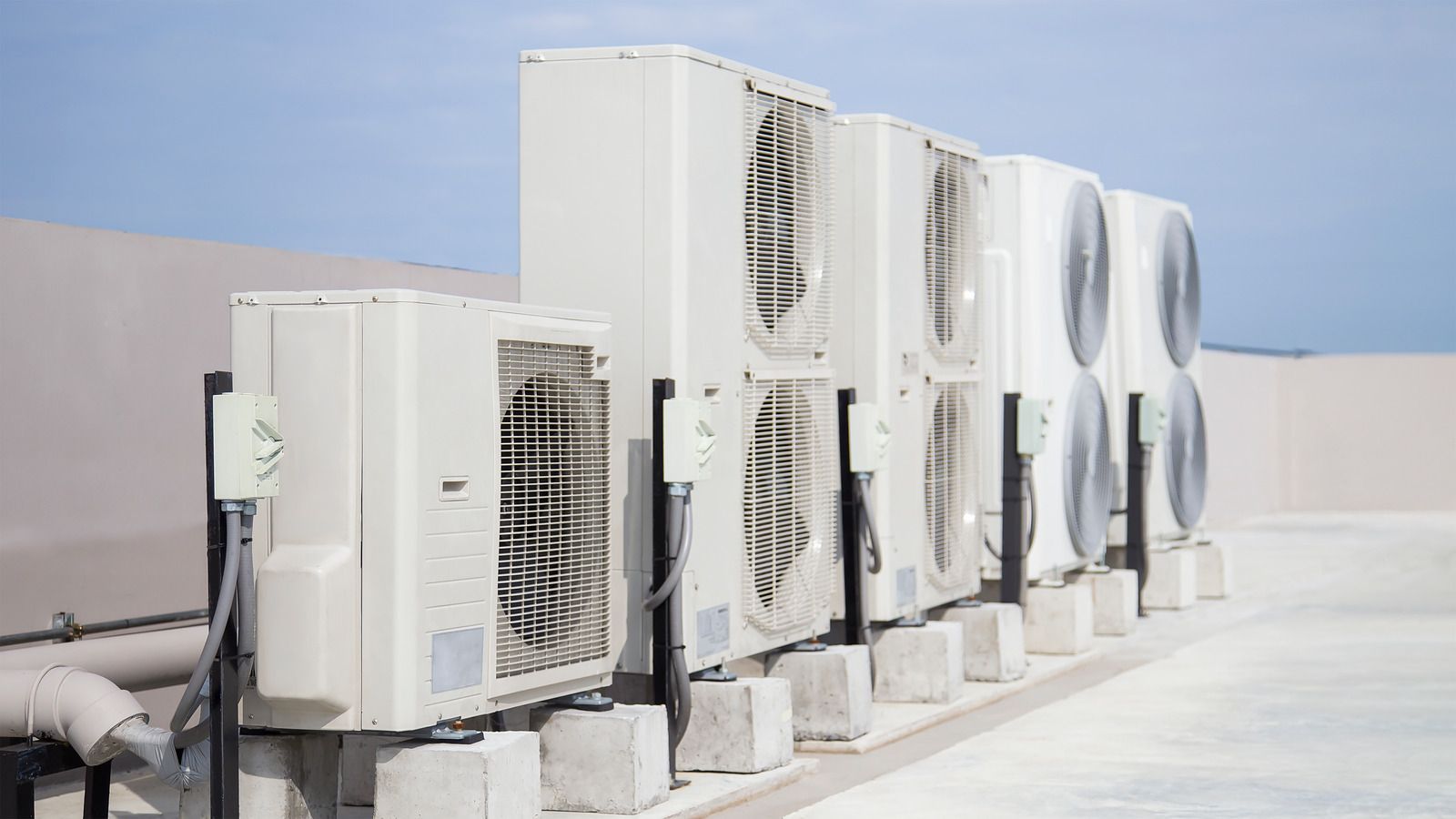 Row of white air conditioning units on a rooftop, against a bright sky.