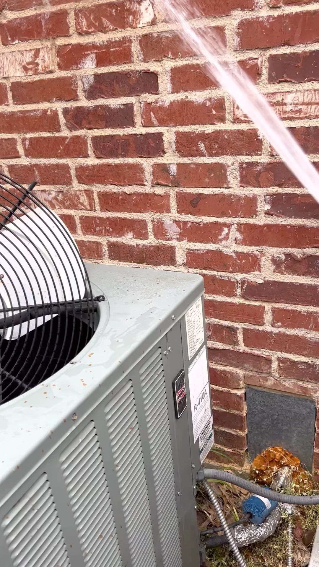 An air conditioner is sitting in front of a brick wall.