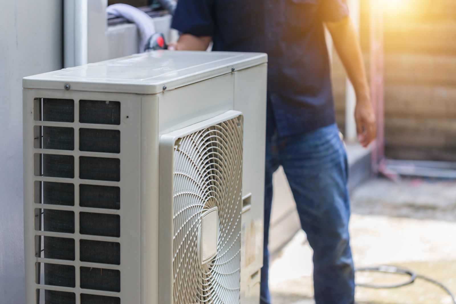 A person installs an air conditioning unit outdoors, near a building.