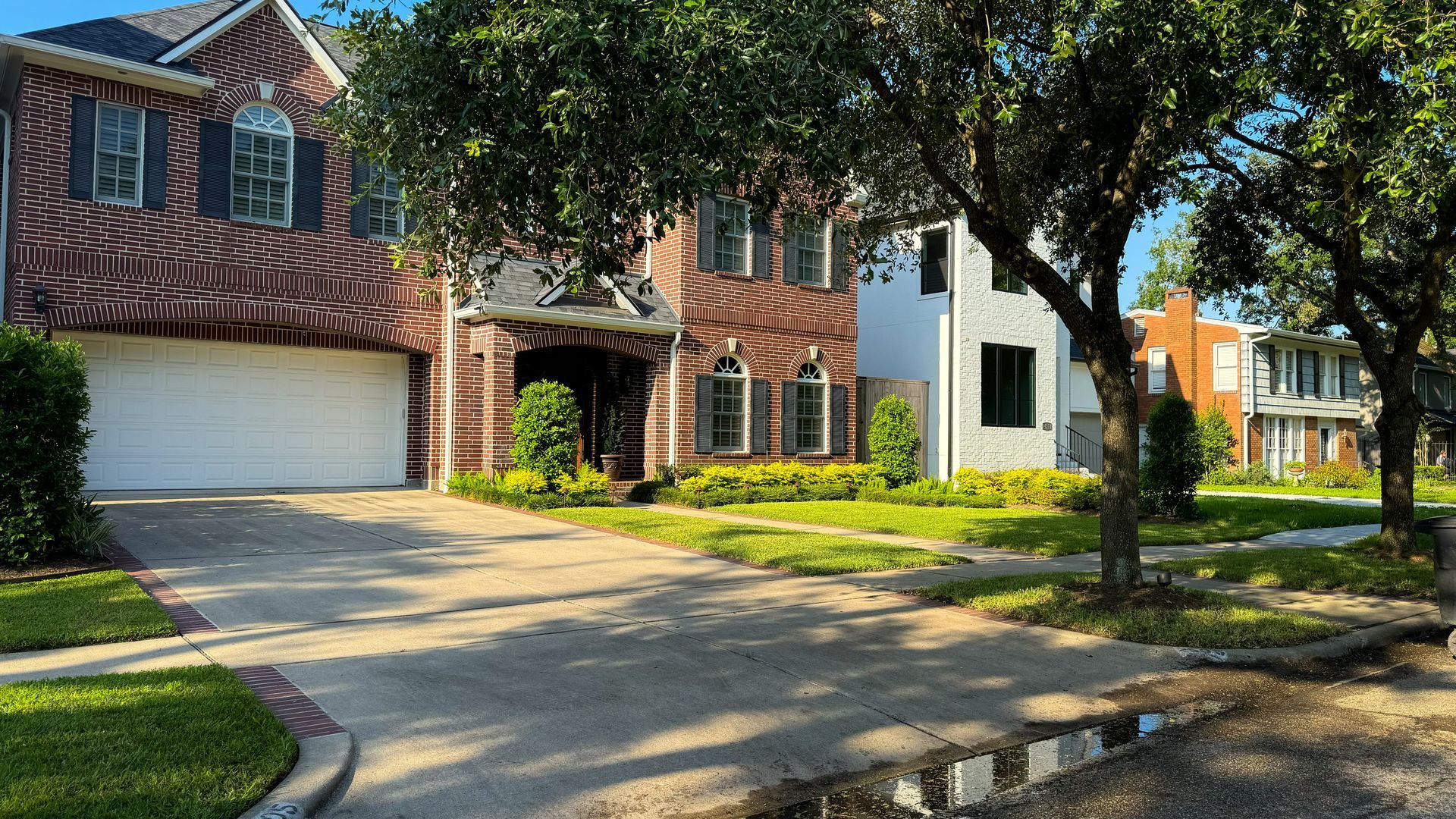 A large brick house with a white garage door is in a residential neighborhood.