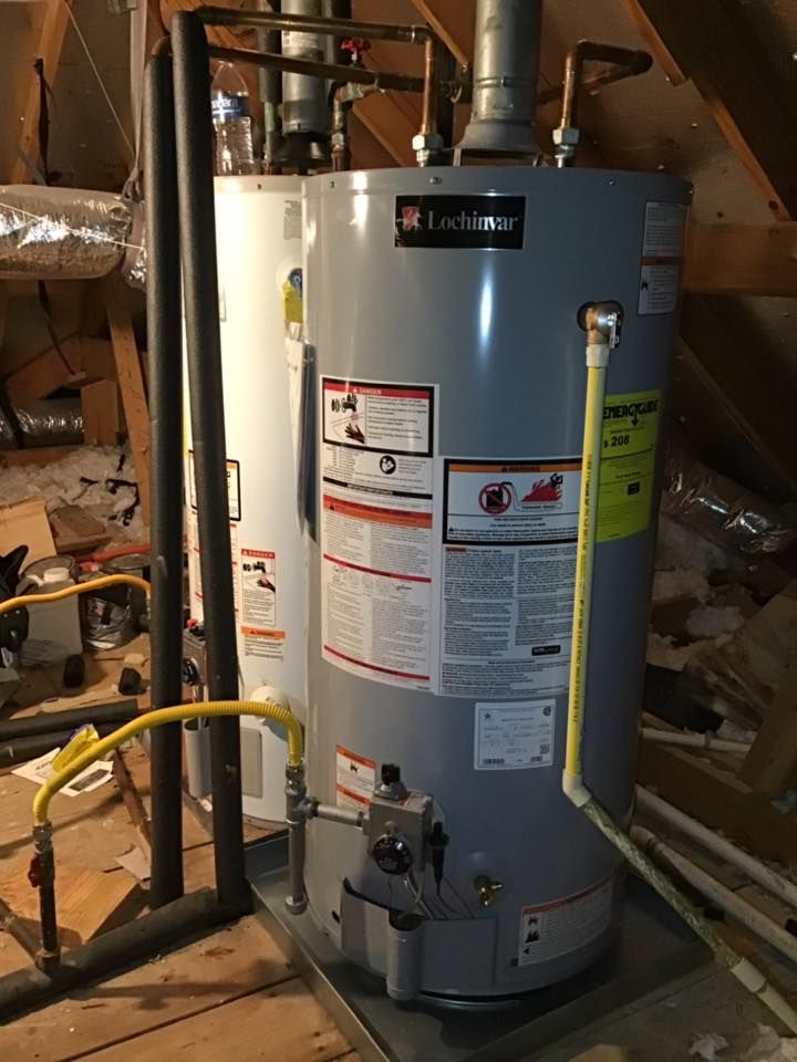 A gas water heater is sitting on top of a wooden floor in an attic.