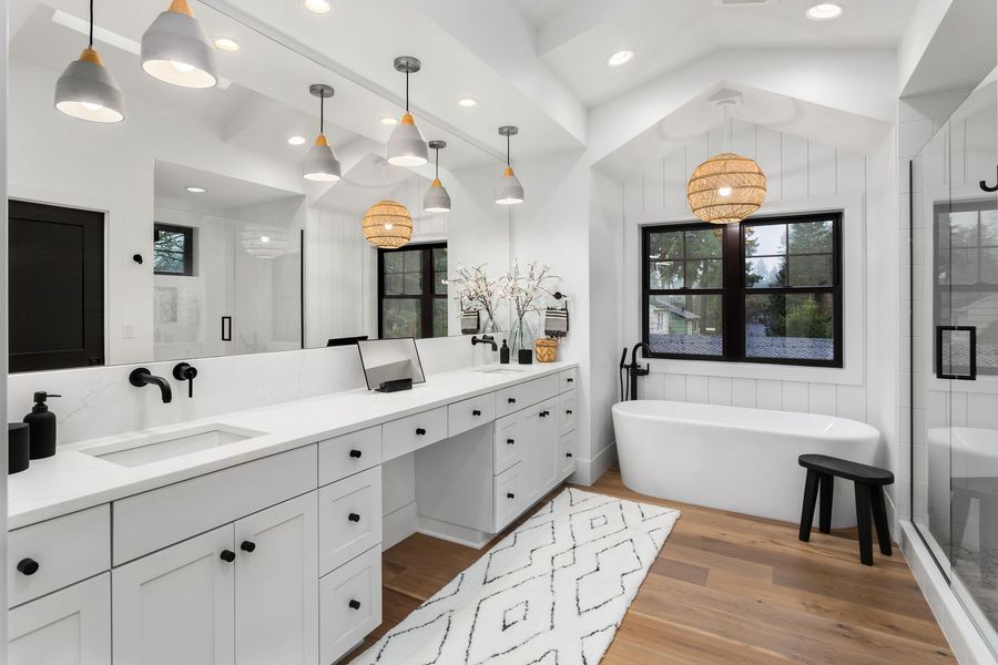 A bathroom with two sinks , a tub , and a large mirror.