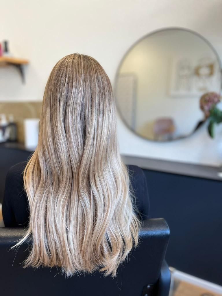 Eine Frau mit langen blonden Haaren sitzt auf einem Stuhl vor einem Spiegel.