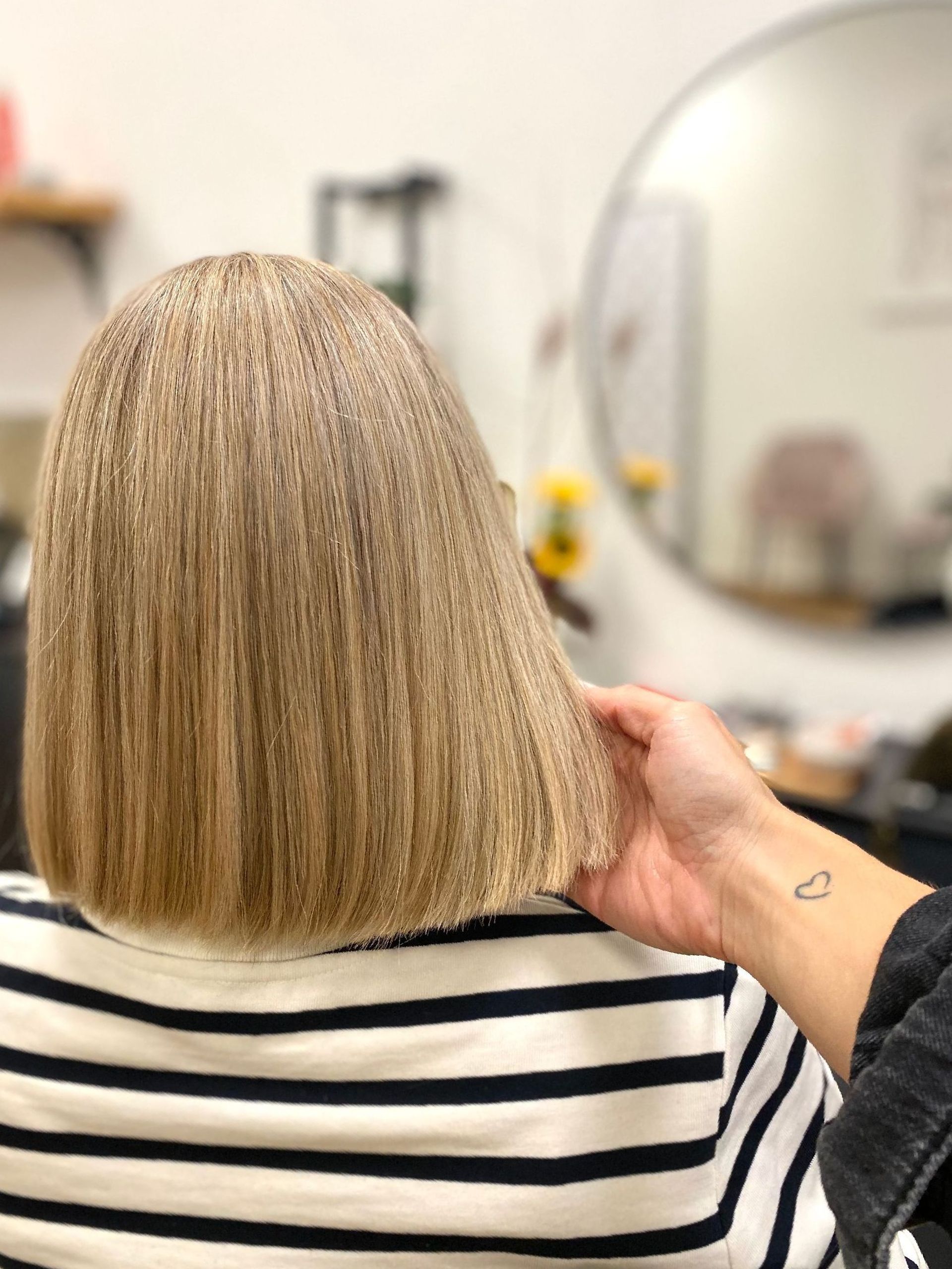 Eine Frau in einem gestreiften Hemd lässt sich von einem Friseur die Haare schneiden.