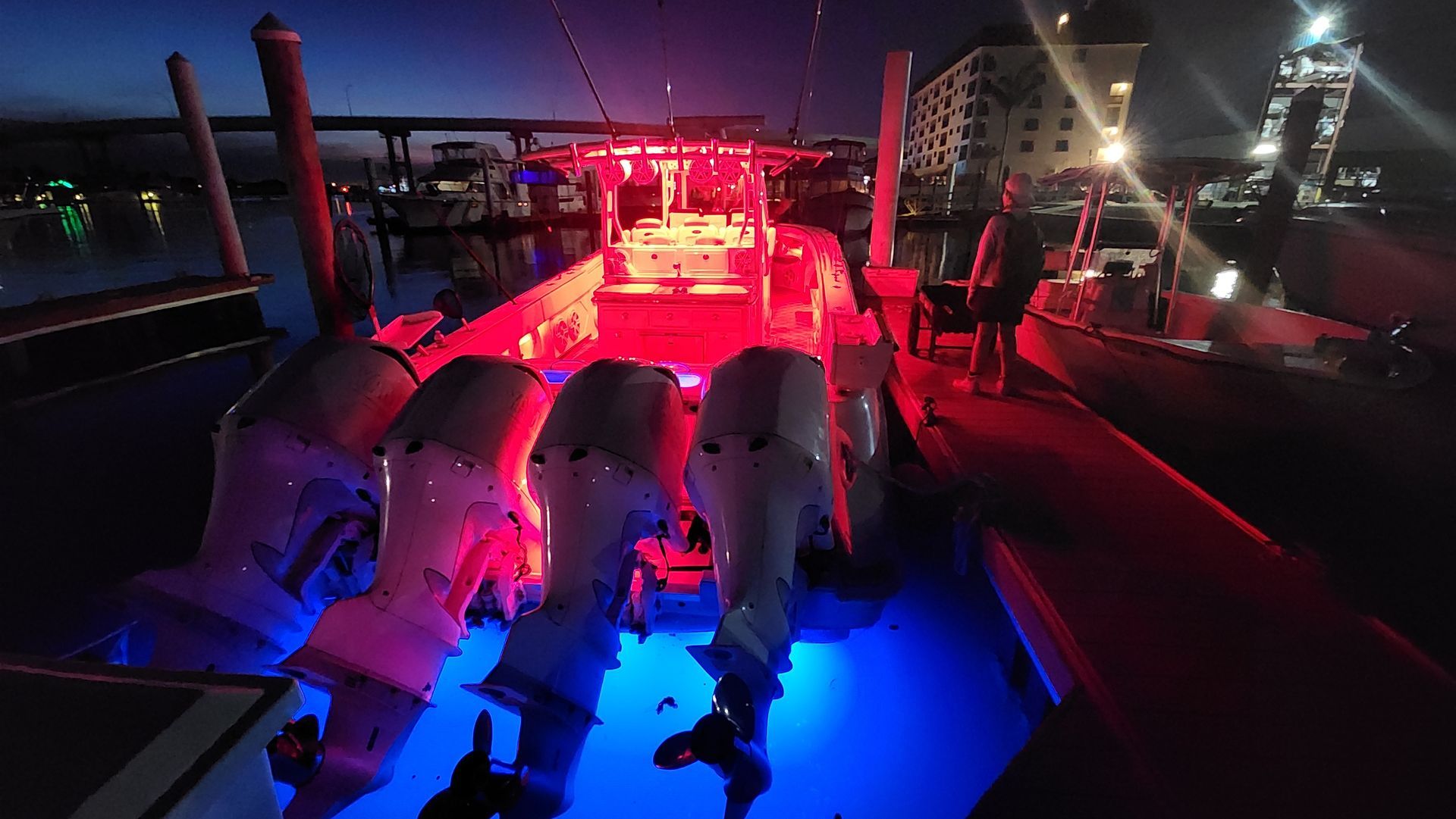 A large boat lit with red and blue lights at night, docked next to a pier.