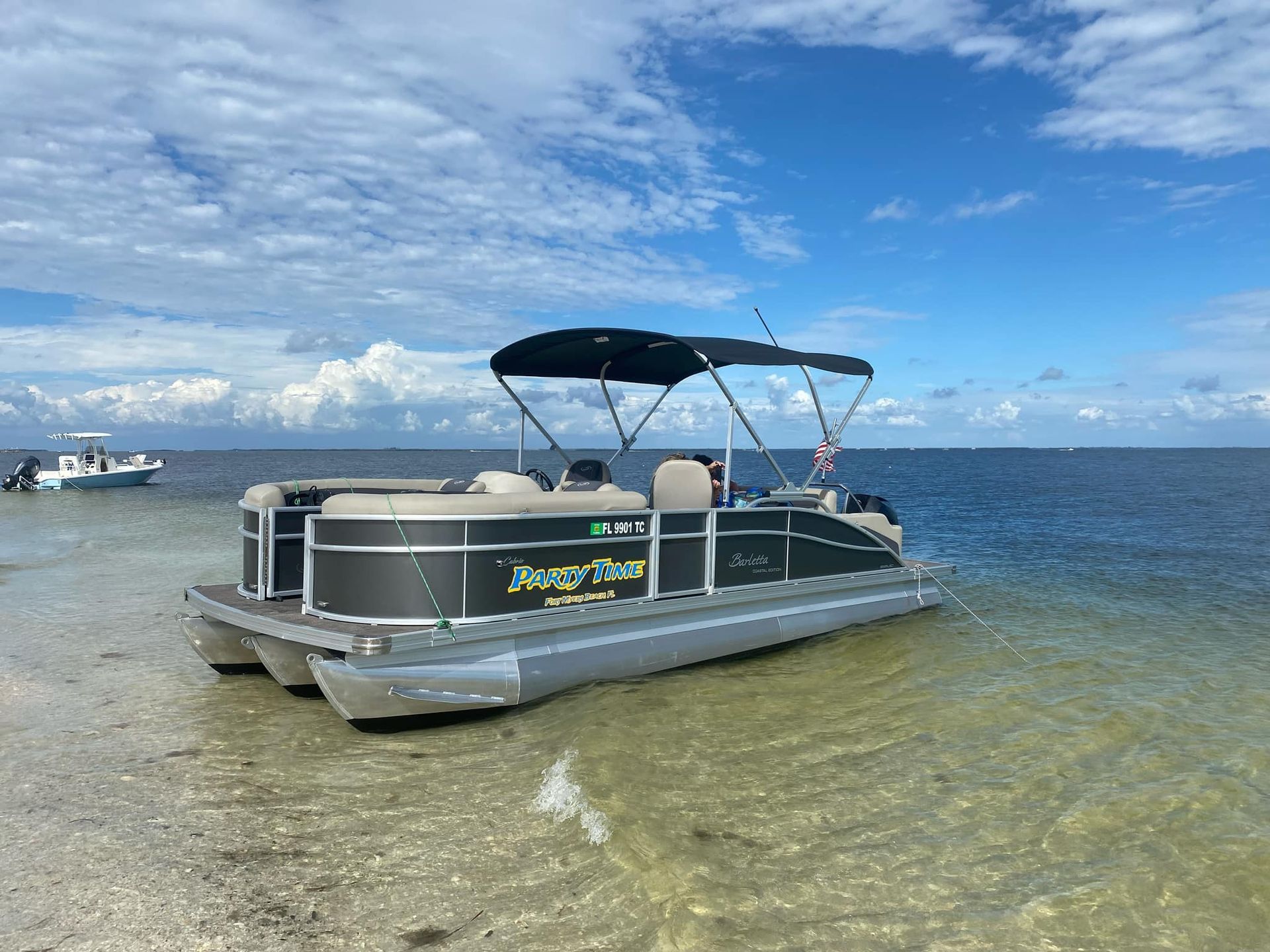 A black pontoon boat beached on a sandy shore under a blue sky.