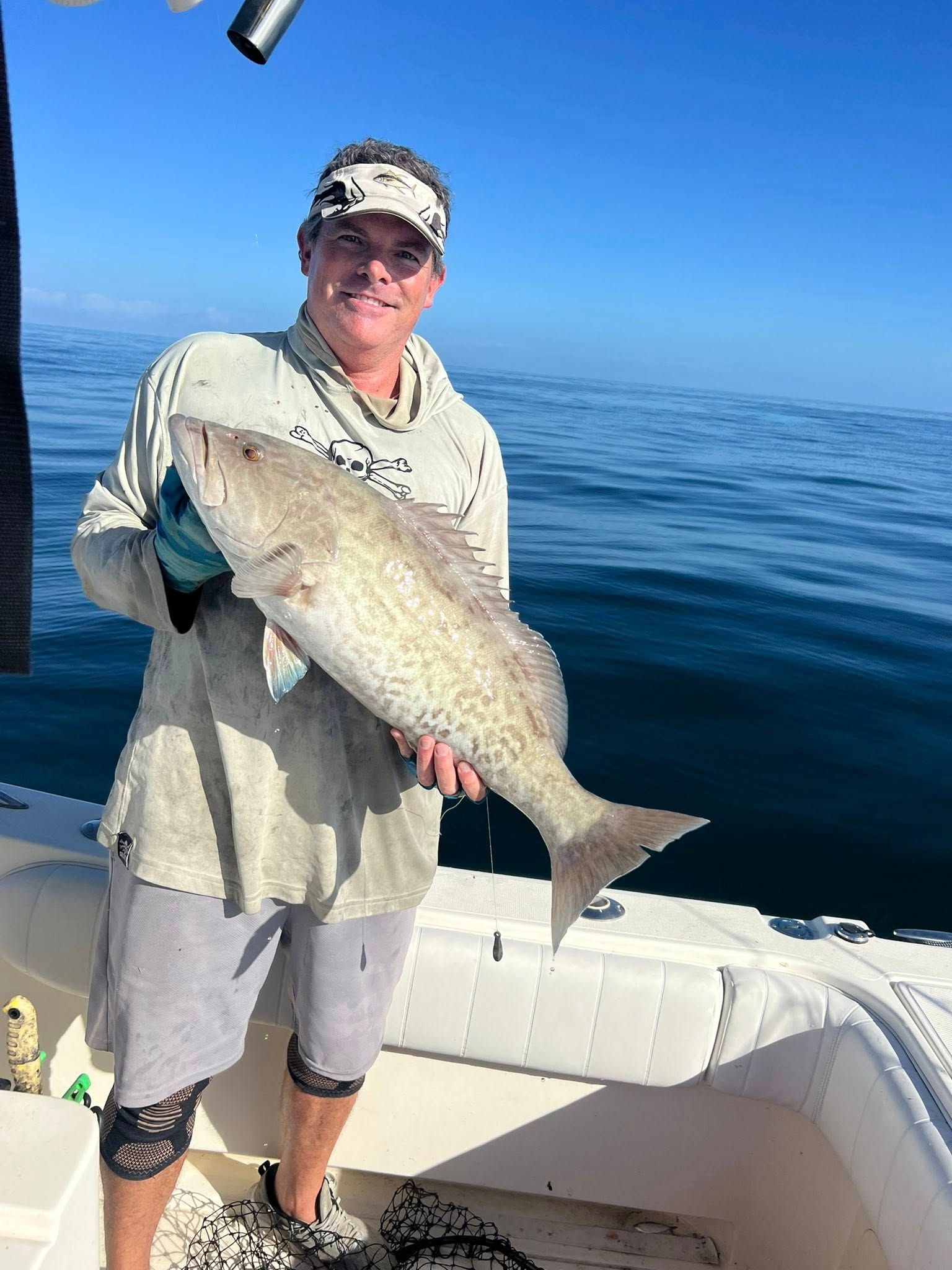 Man on boat holds up large fish against a blue sky and sea.
