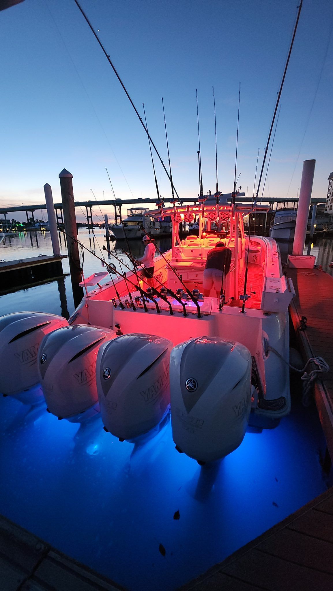 Boat at a dock with red and blue lights at dusk, with people on board.