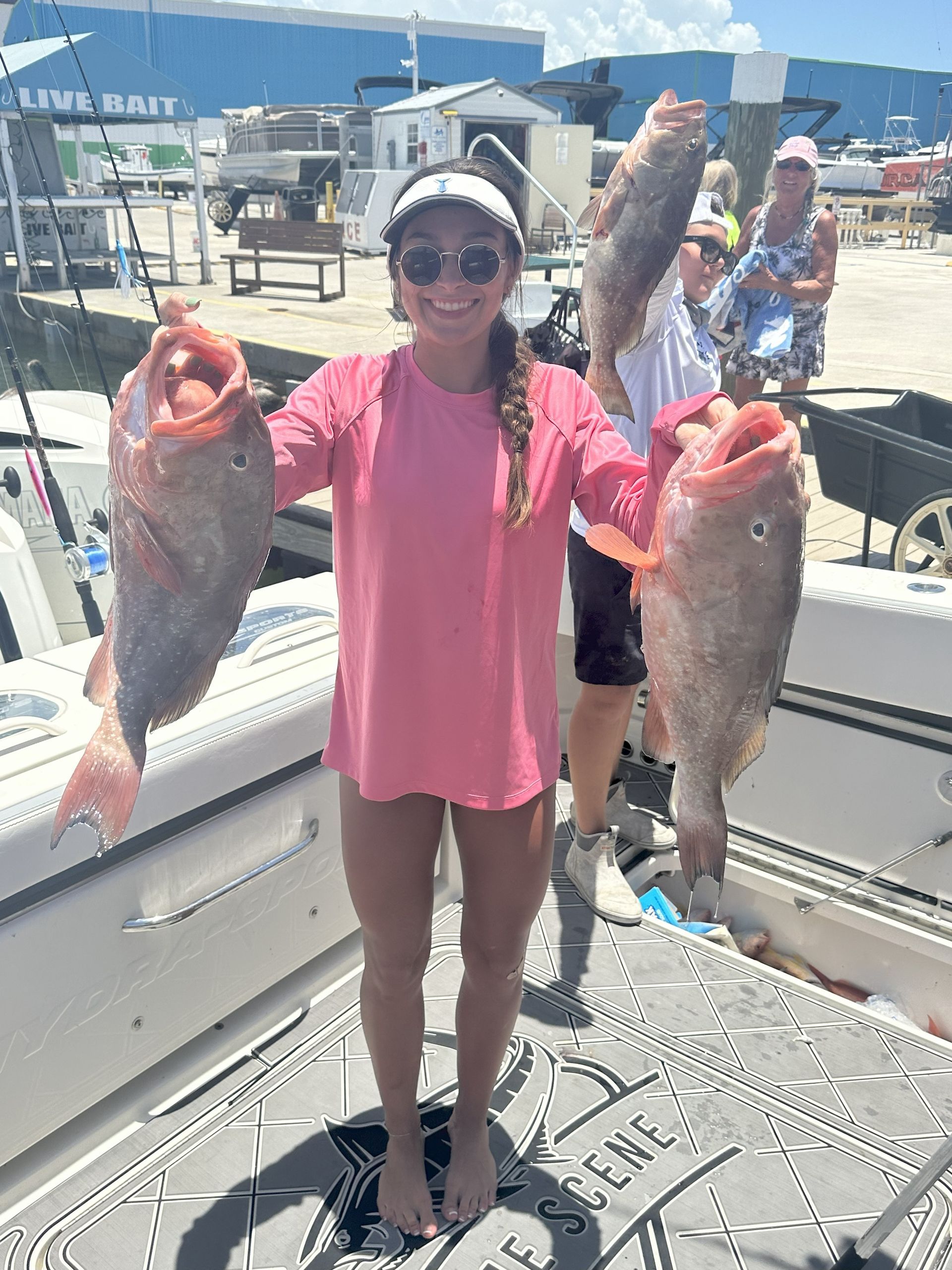 Woman on boat holds up two large red fish; sunny day.
