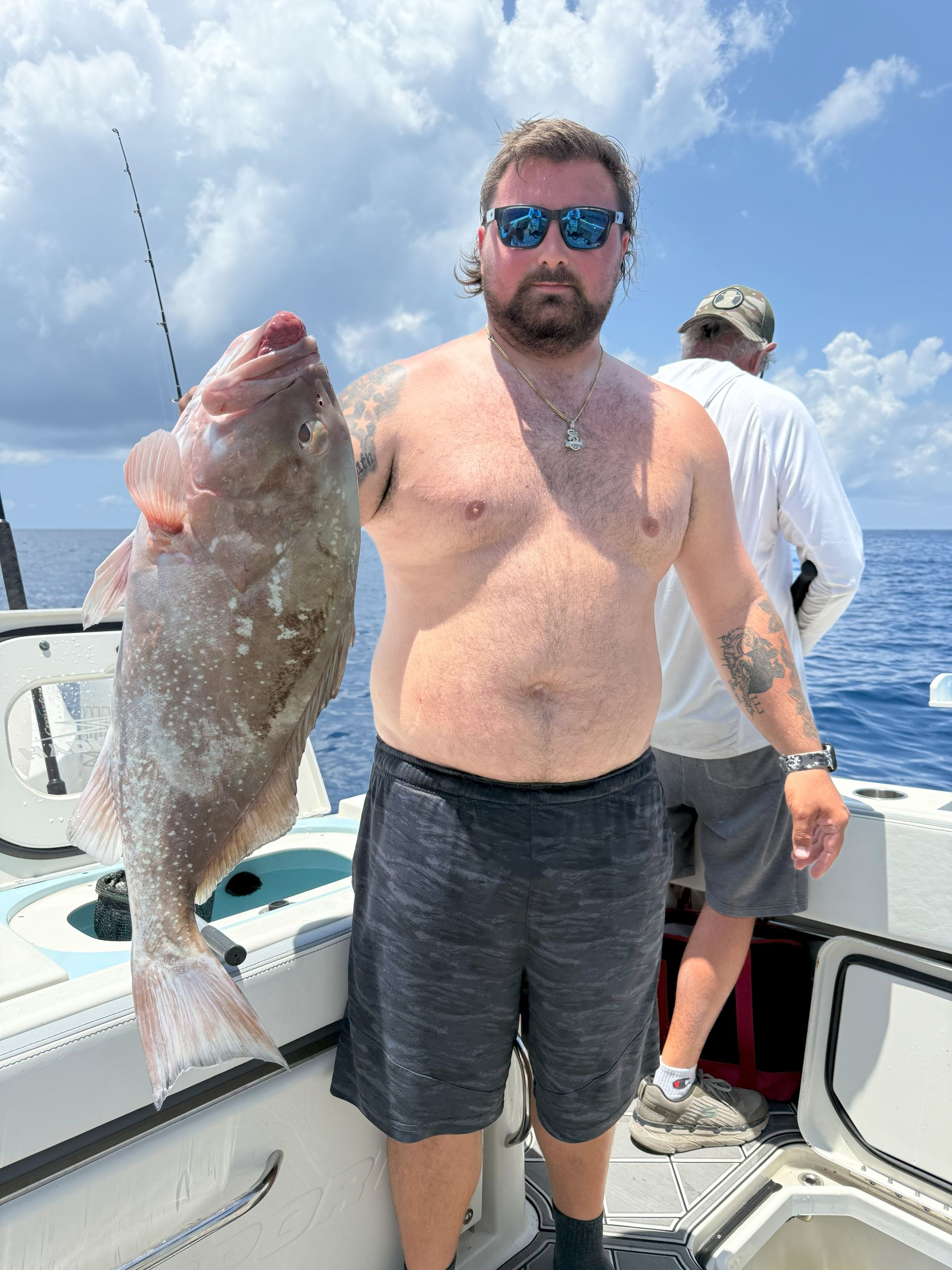 Man holding a large pink fish on a boat, blue water and sky in the background.