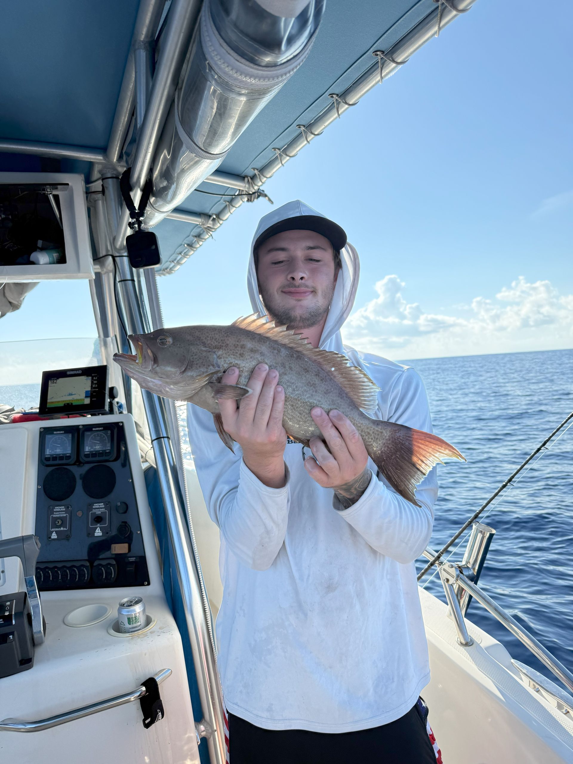 Man on a boat holds a red snapper he caught, smiling with the ocean in the background.