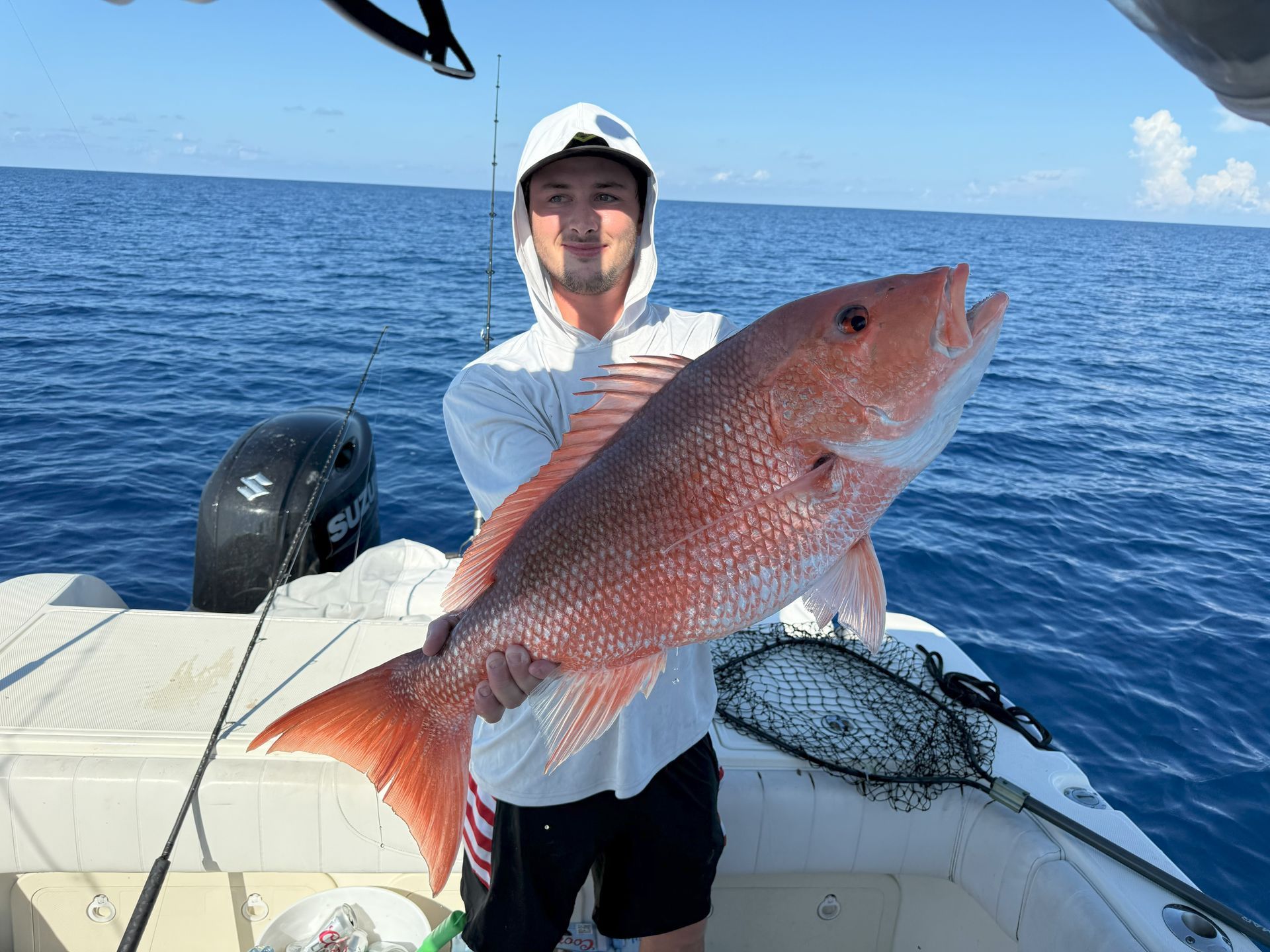 Man on a boat holding a large red snapper fish, blue water and sky background.