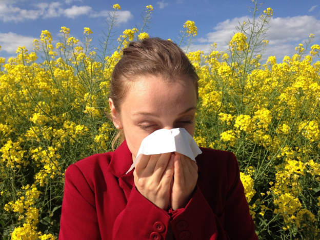 A woman is blowing her nose in front of a field of yellow flowers.