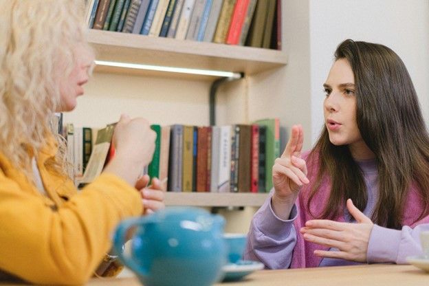 Two women are sitting at a table talking to each other in sign language