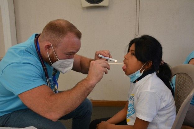 A doctor is examining a child 's throat with a thermometer.