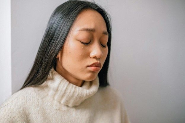 A woman in a white sweater suffering from blocked ears is looking down with her eyes closed.