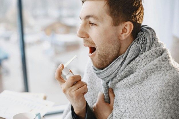 A man wrapped in a blanket using an oral spray.