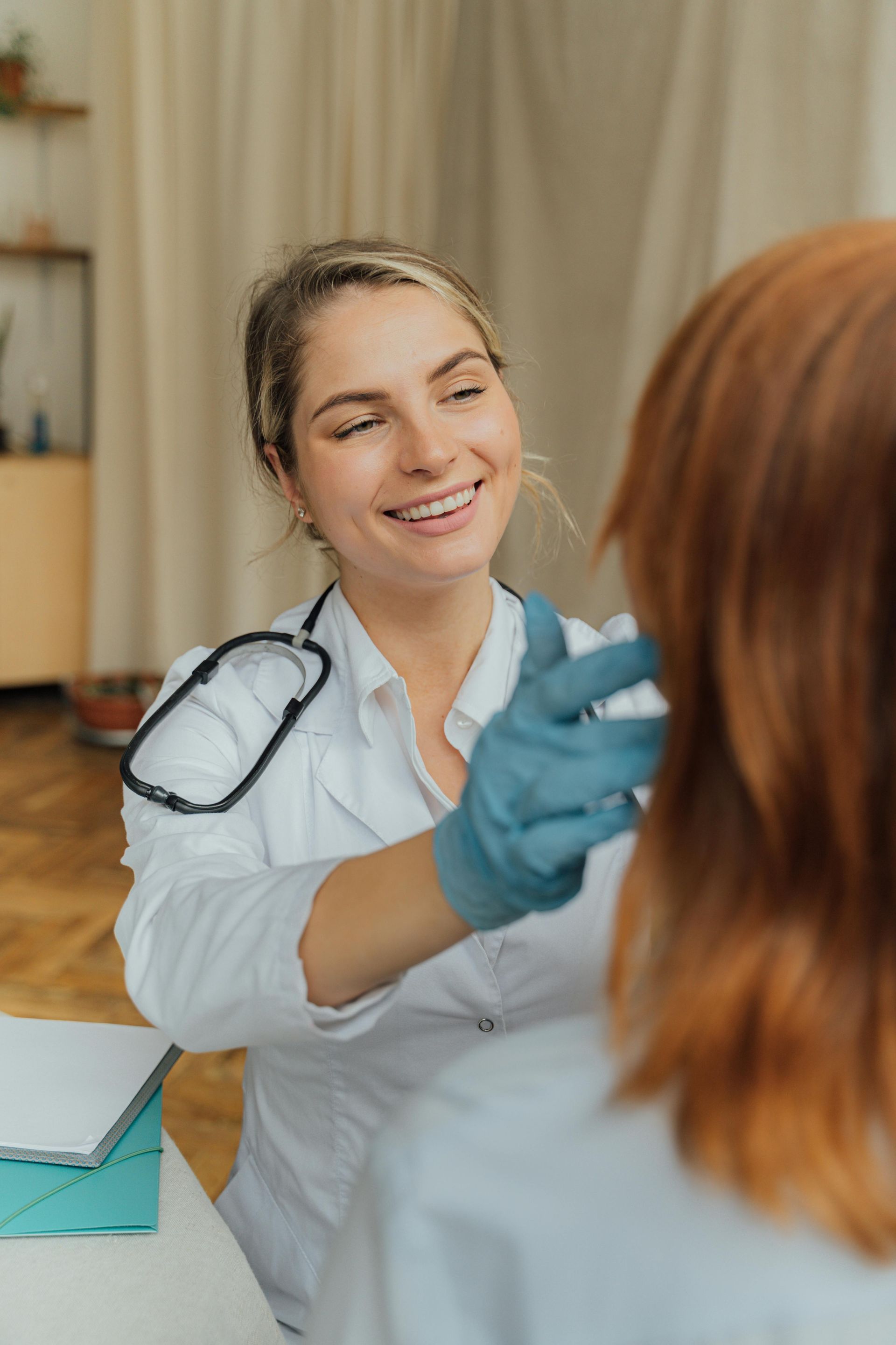 Doctor smiling while examining a patient in a clinic using blue gloves and a stethoscope