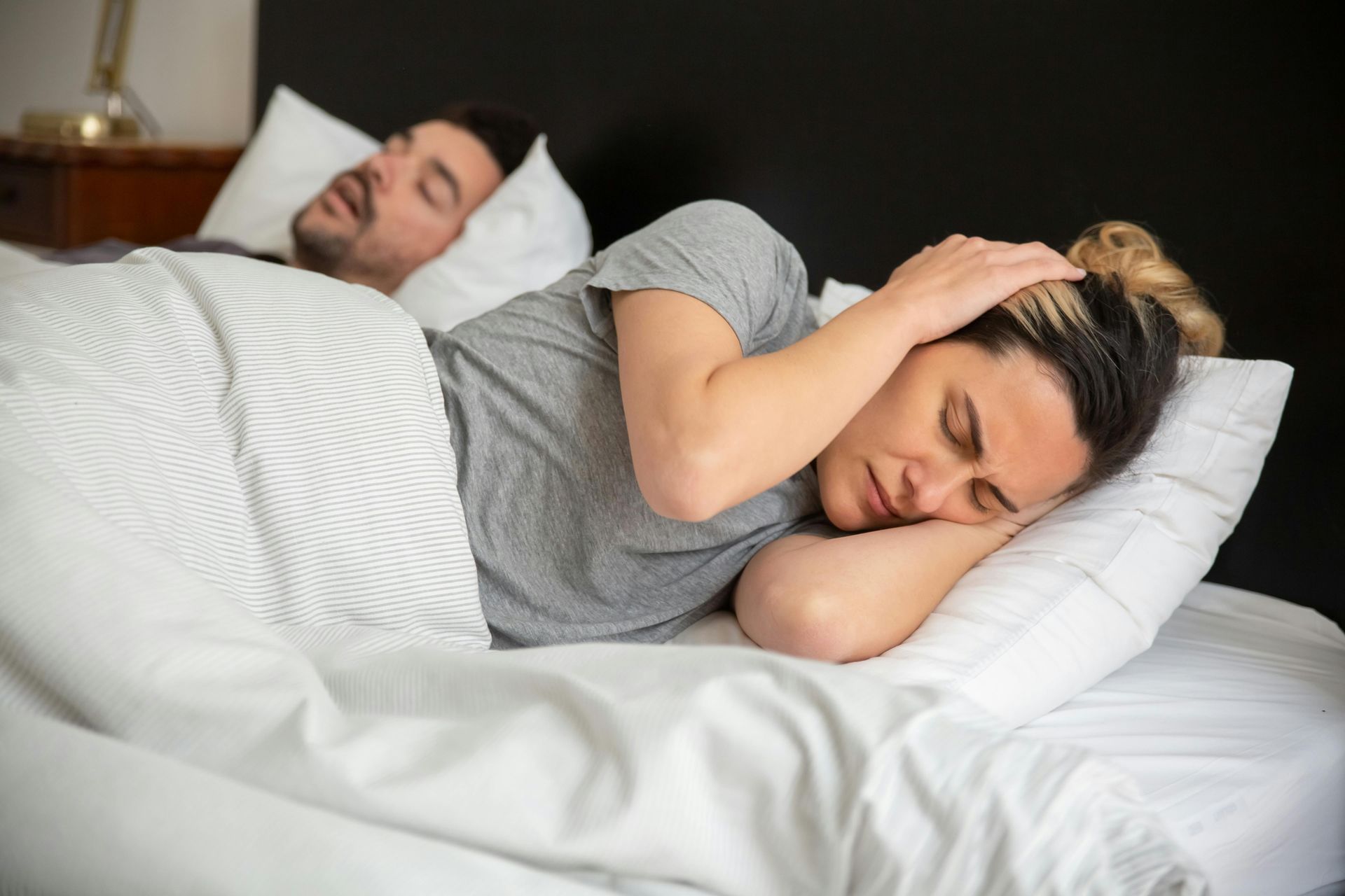 A woman is covering her ears while a man snores in the background.