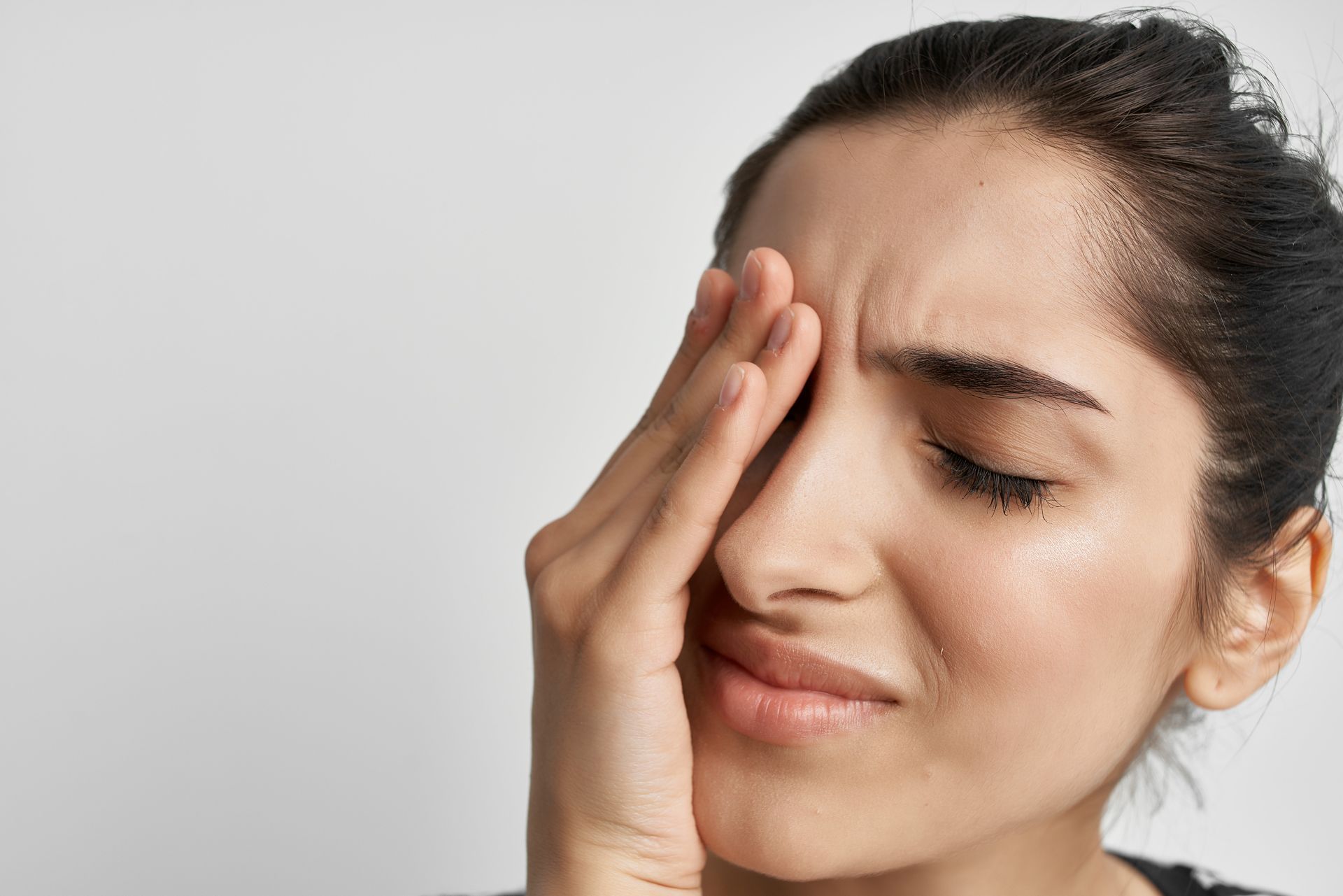 A woman with sinus tumor is holding her hand to her forehead because she has a headache.