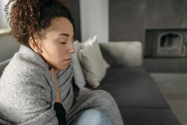 A woman is sitting on a couch wrapped in a blanket.