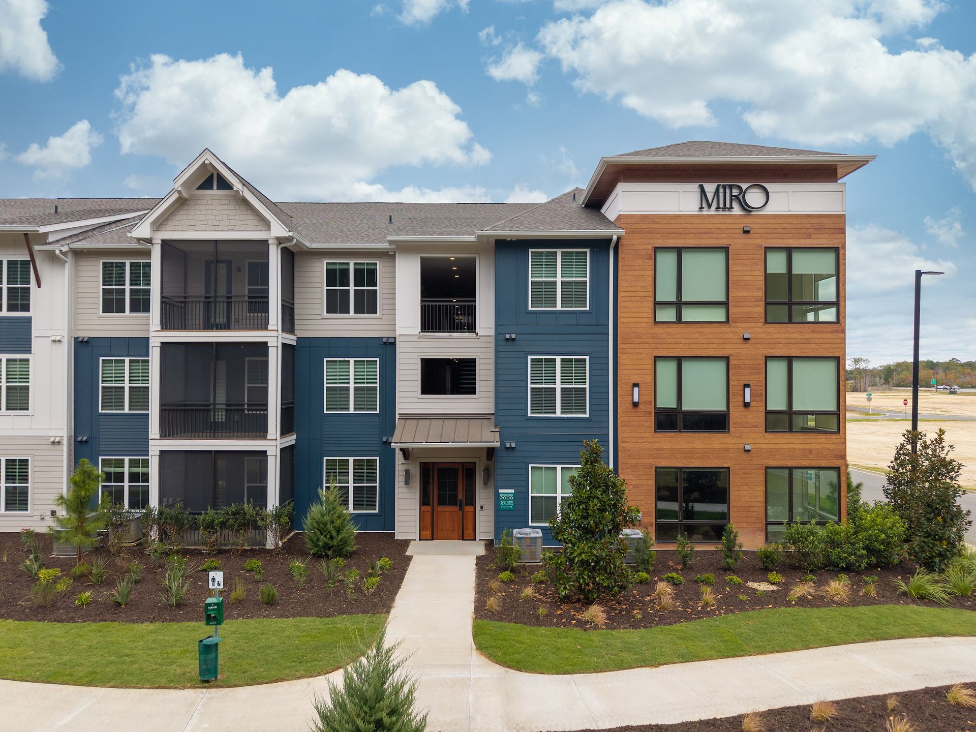 Apartment building exterior, featuring blue and brown siding. Pathway leads to the front entrance. 