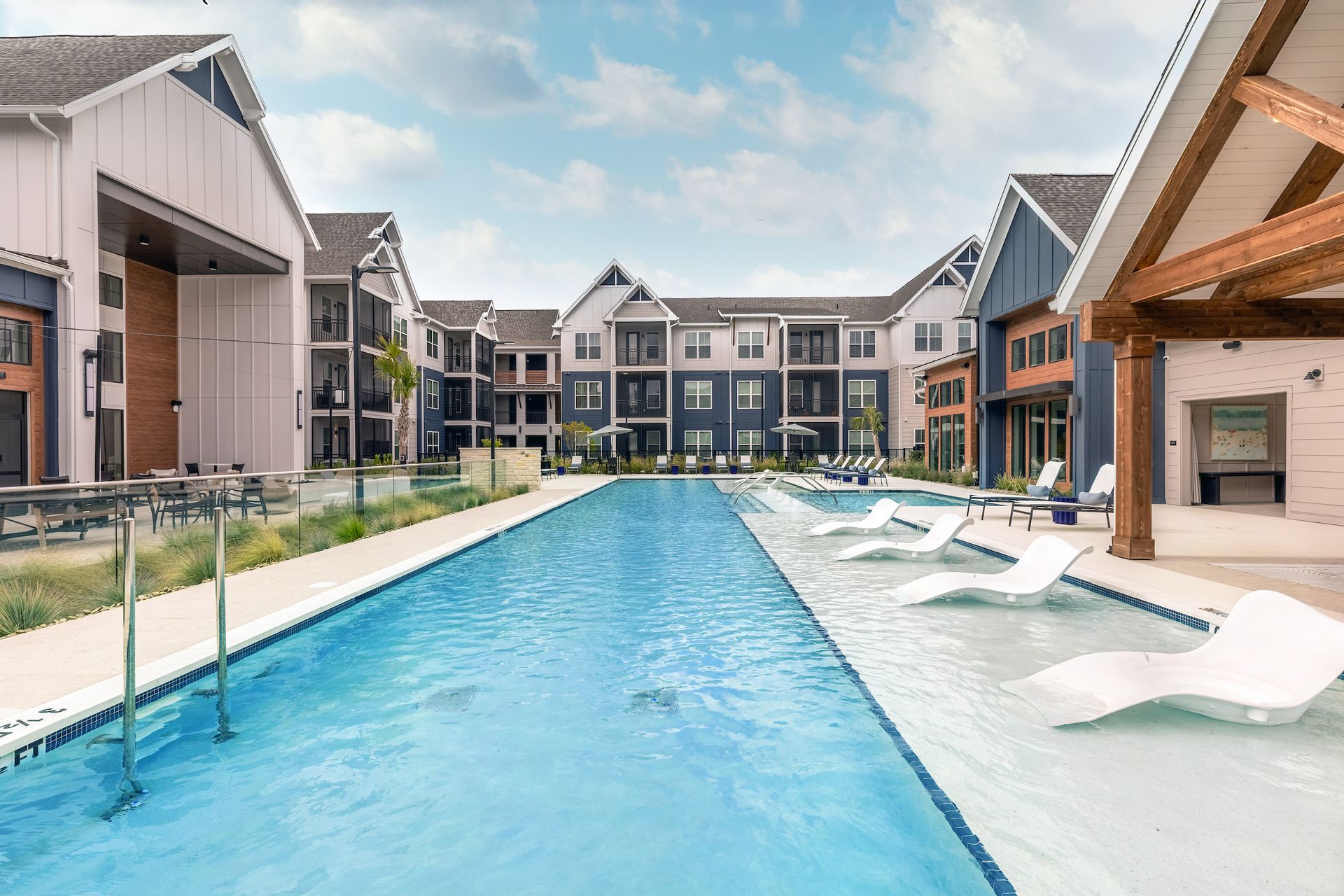 Swimming pool and lounge chairs in front of apartment buildings with white and blue siding.