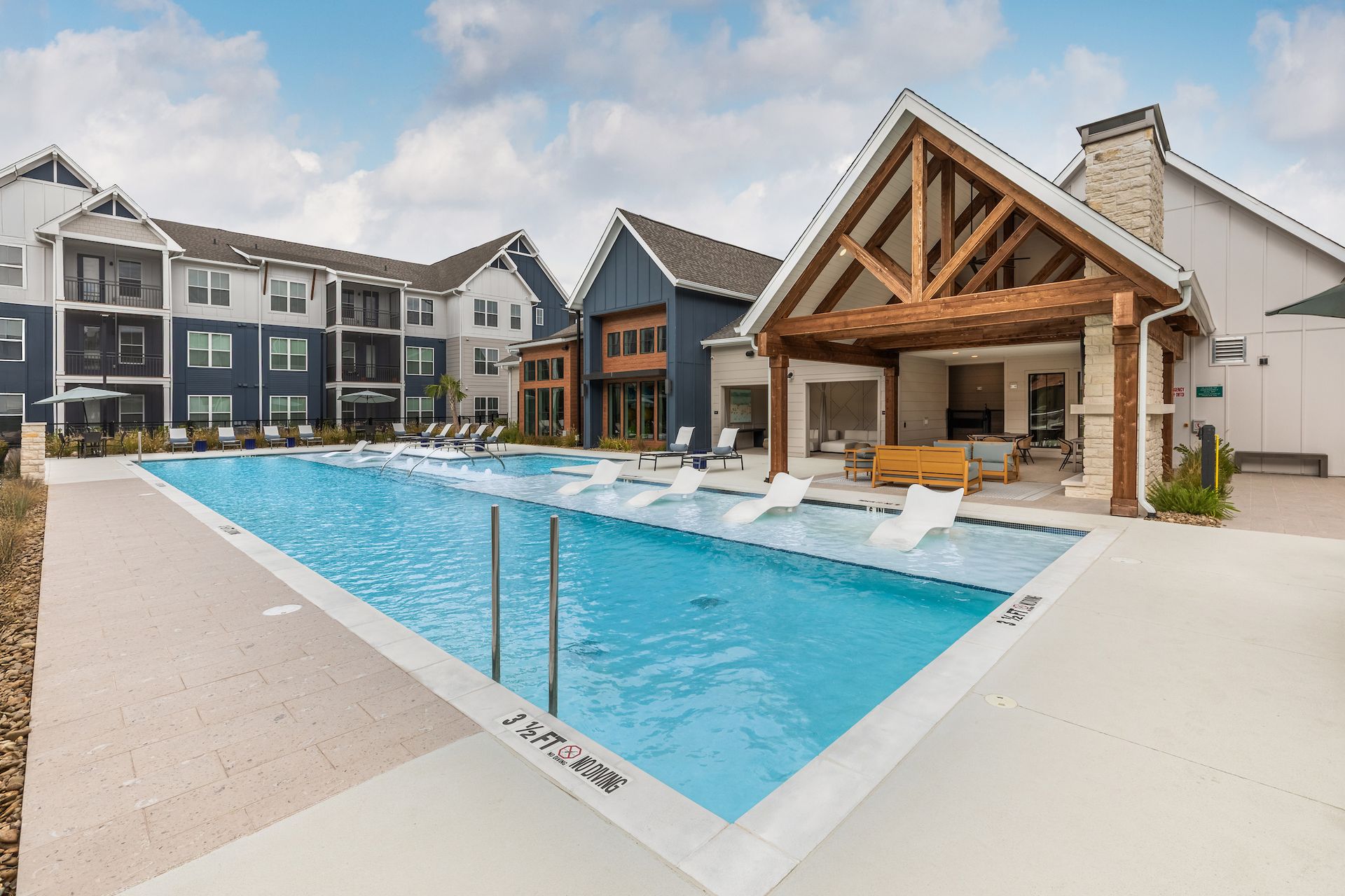 Swimming pool at apartment complex with lounge chairs and shaded seating area.
