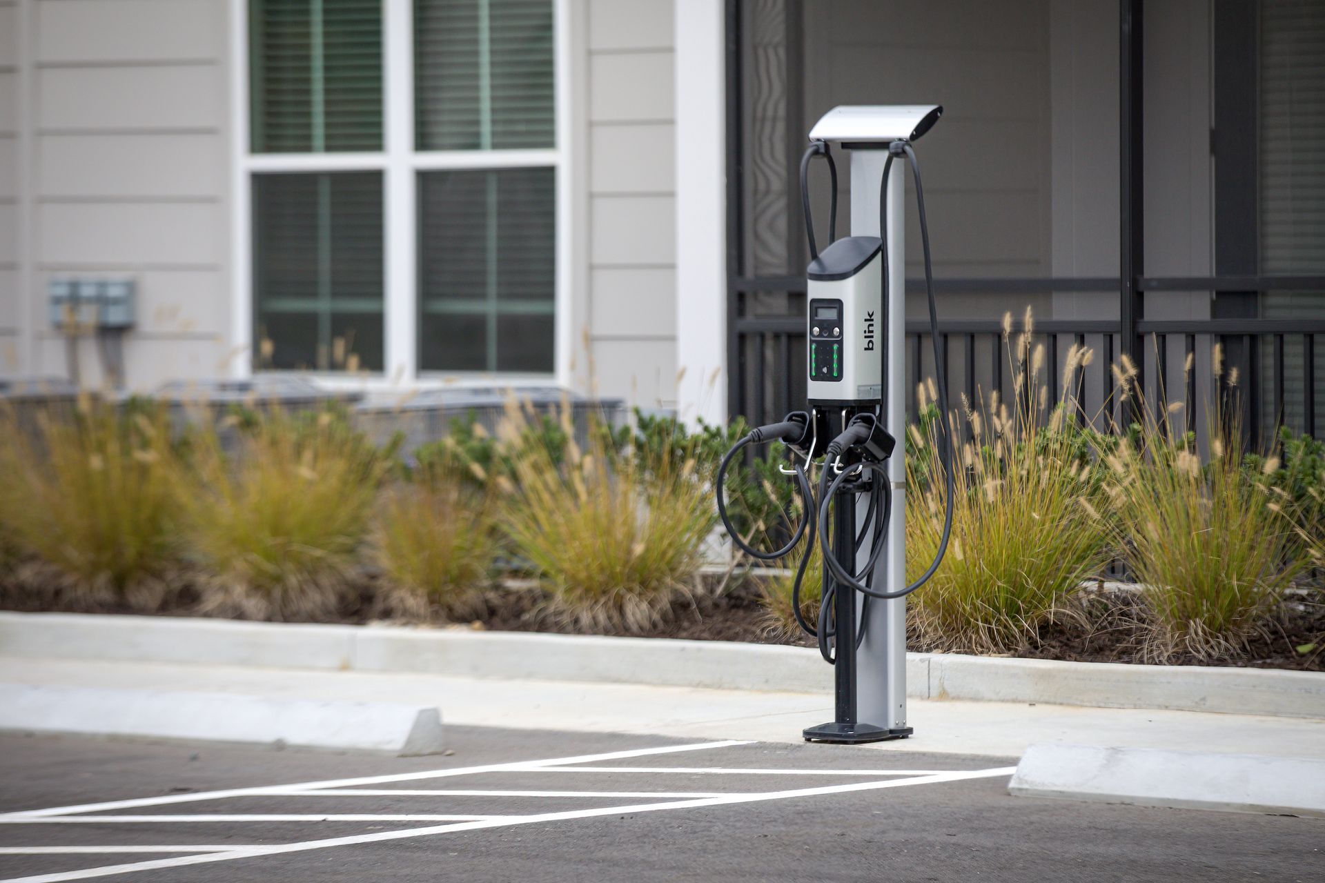 EV charging station on a parking space, near a building with tan siding and windows, grass in the background.