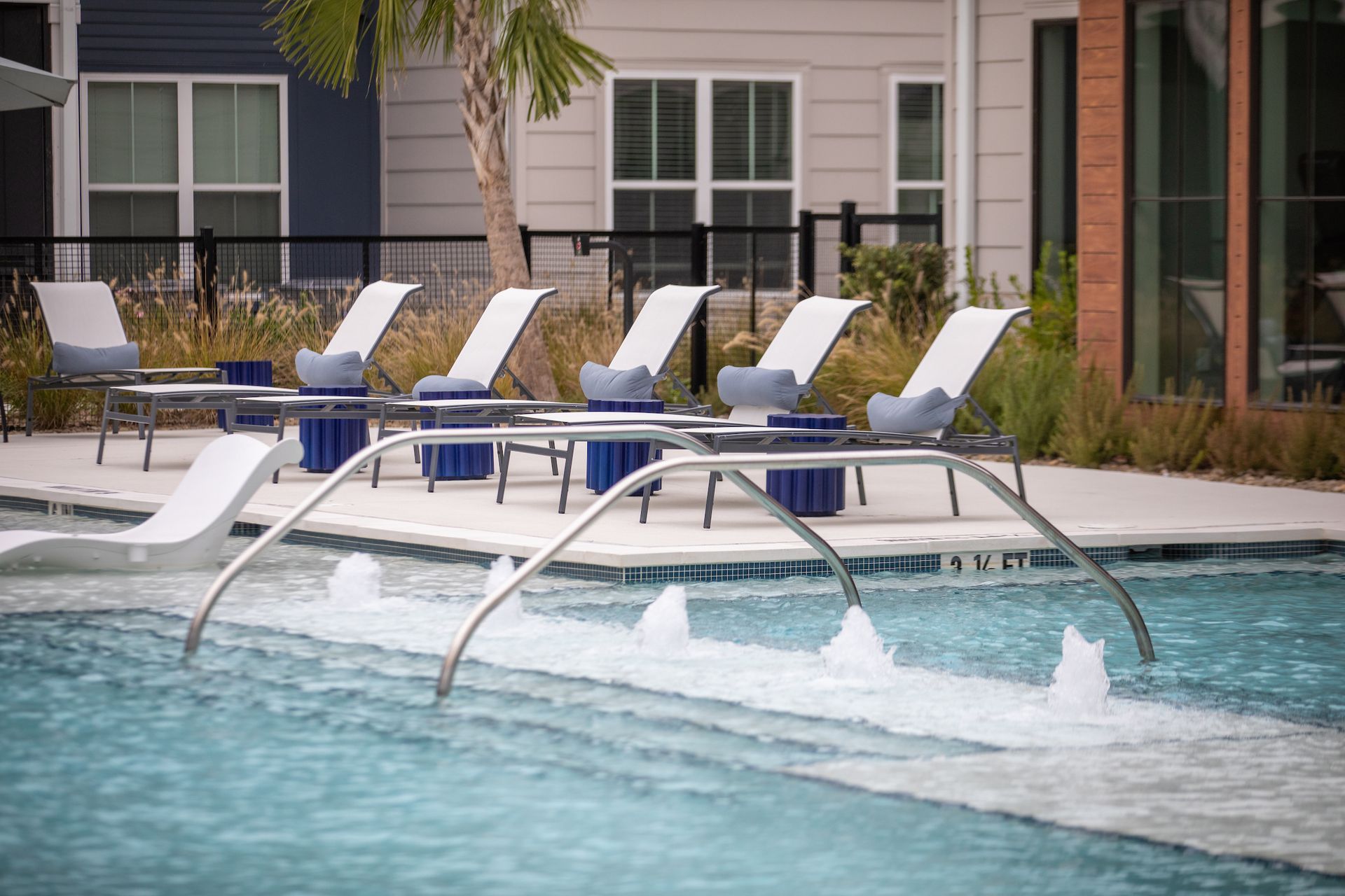 Swimming pool with jets, lounge chairs, and building in the background.