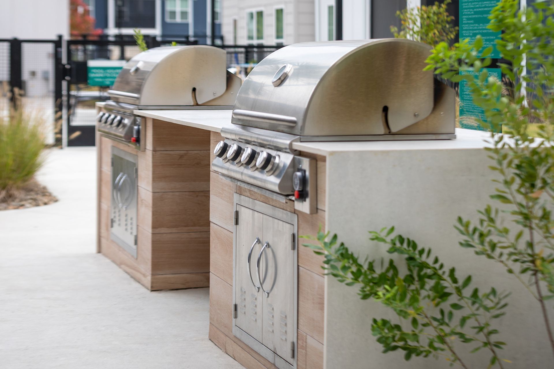 Two stainless steel grills on concrete and wooden structures outside near greenery.
